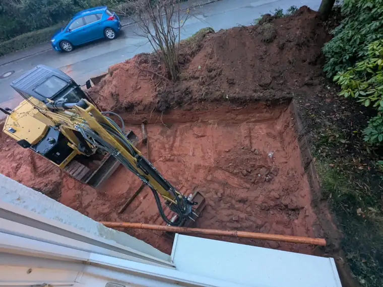 Minibagger in einer Baugrube direkt neben einem Wohnhaus